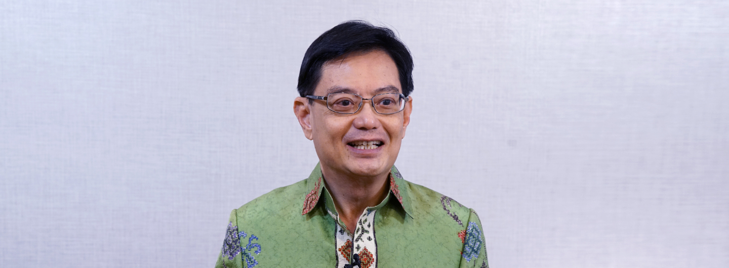 Man in glasses and a patterned green shirt against a light gray background.